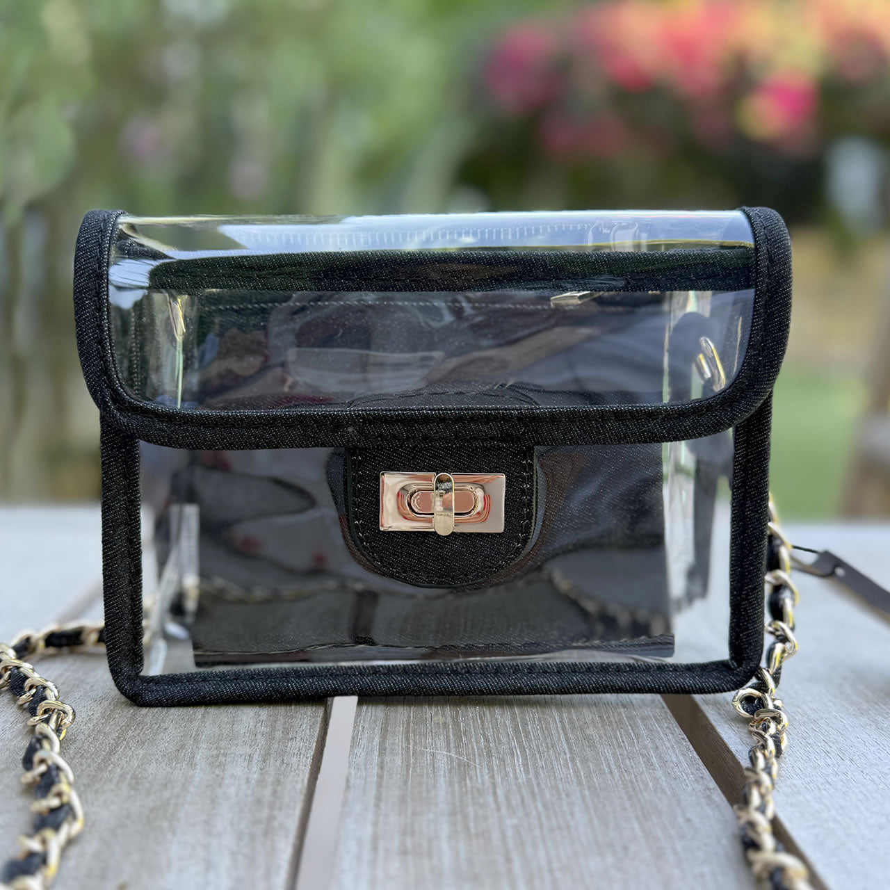 Clear, stadium approved fanny pack with faux-leather navy trim and silver hardware sitting outside on a picnic table