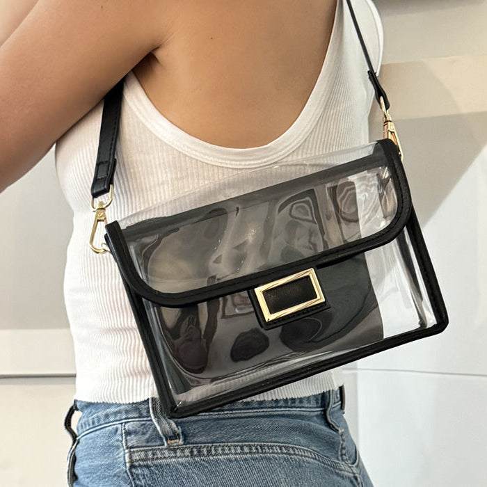 Person wearing a clear handbag with black accents and a black strap.
