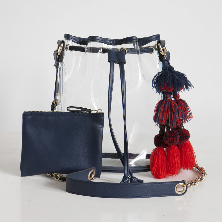 Clear handbag with navy strap and red tassel accessory on a white background