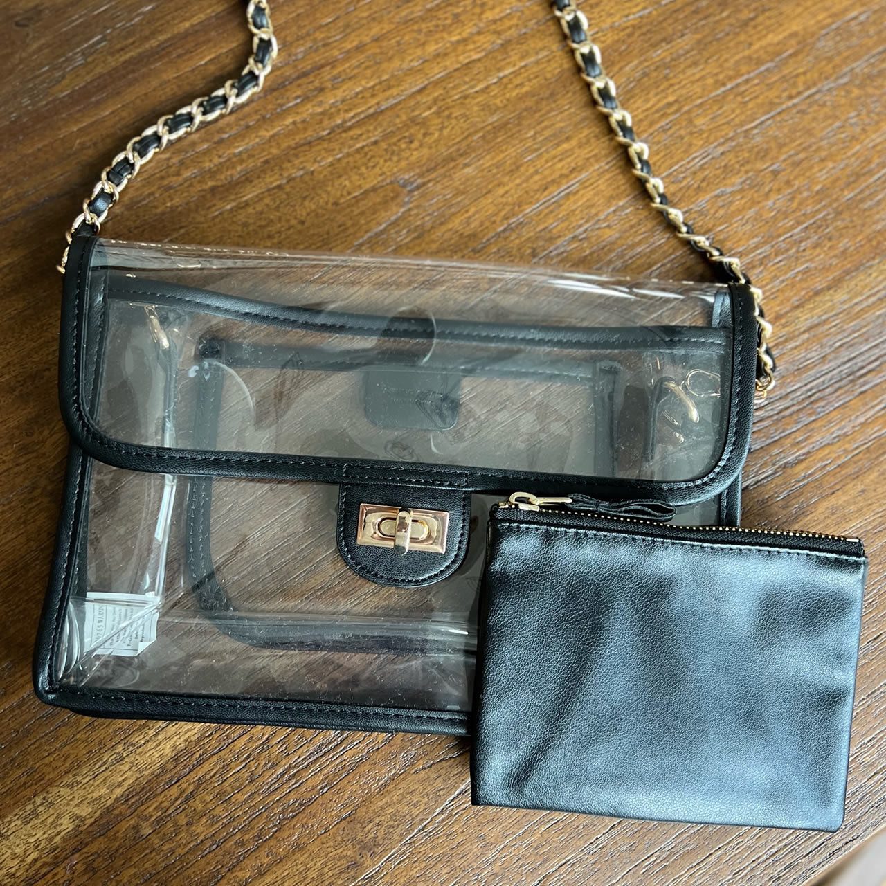 Clear, stadium approved purse with black trim and a gold chain strap
