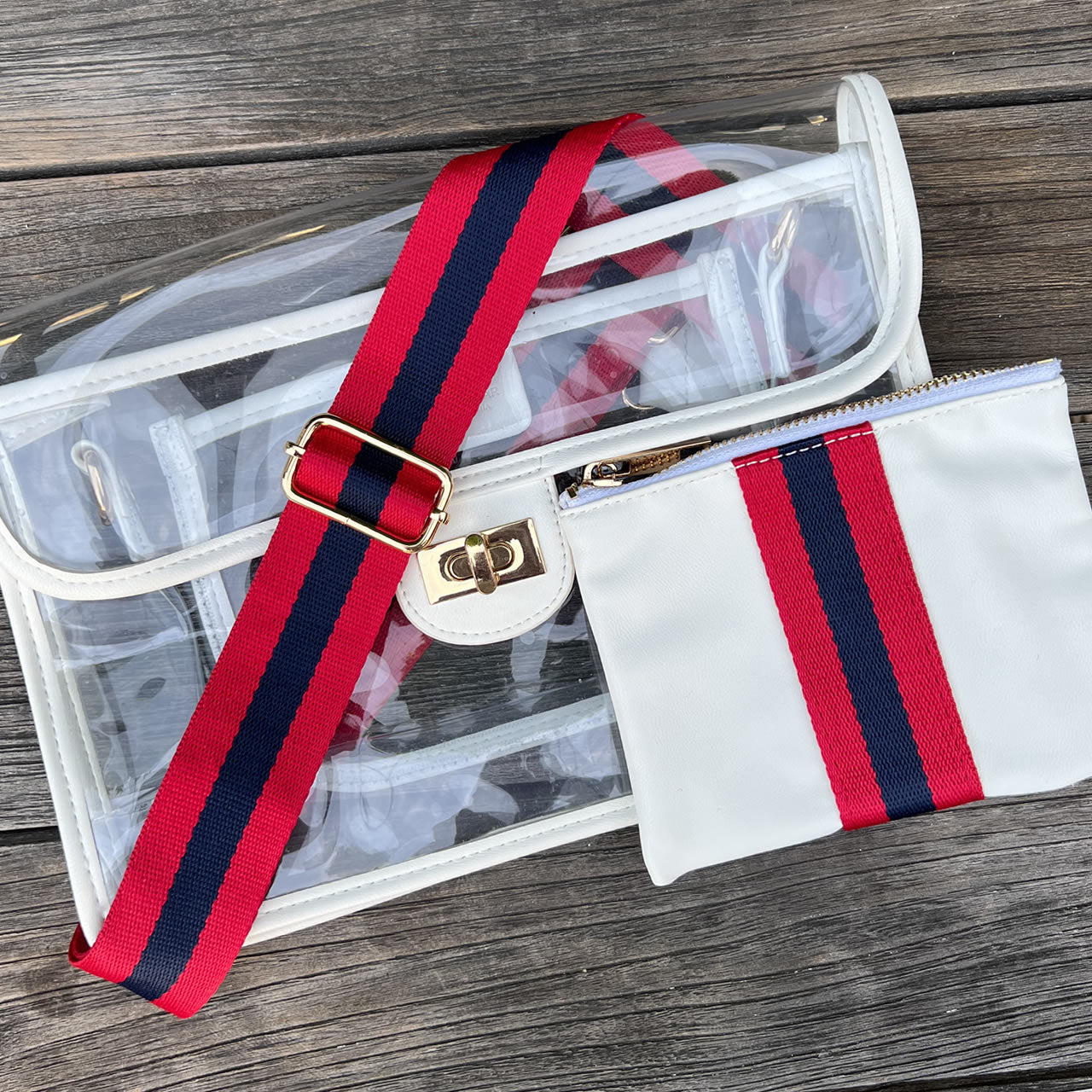 Clear, stadium approved purse with red and navy strap on a wooden surface