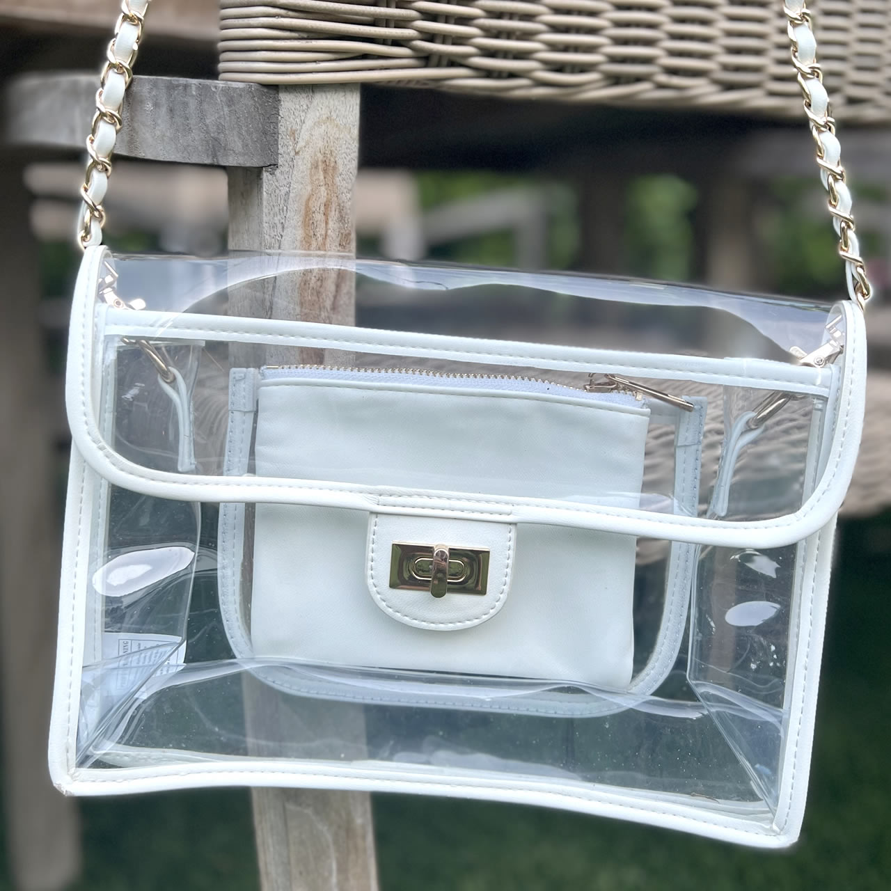 Clear, stadium approved purse with white trim hanging from a gold chain