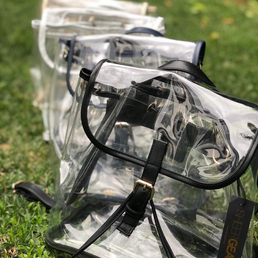 Three stadium approved backpacks in black, white, and navy lined up on the grass