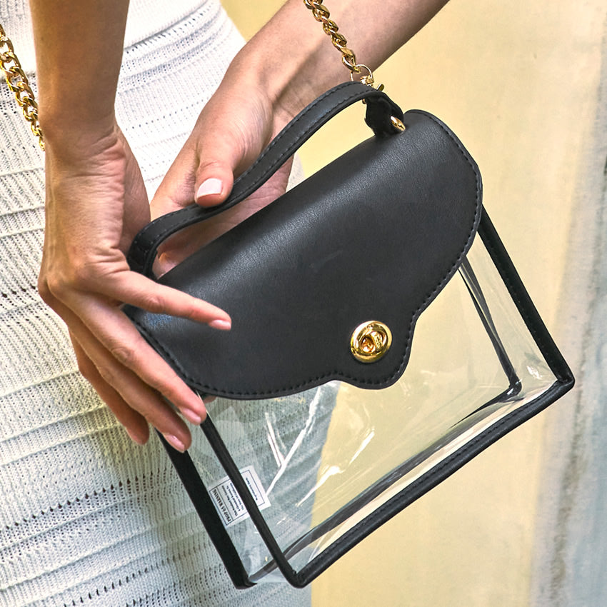 A woman holds a stadium-approved clear purse with black trim and flap.