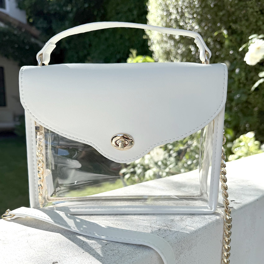 White purse with clear, stadium-approved sides on a stone wall with greenery in the background