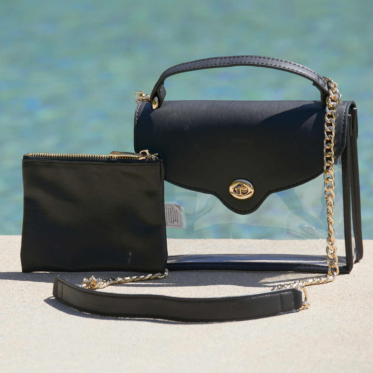 Black, stadium approved purse with gold chain and matching pouch sitting by the pool.