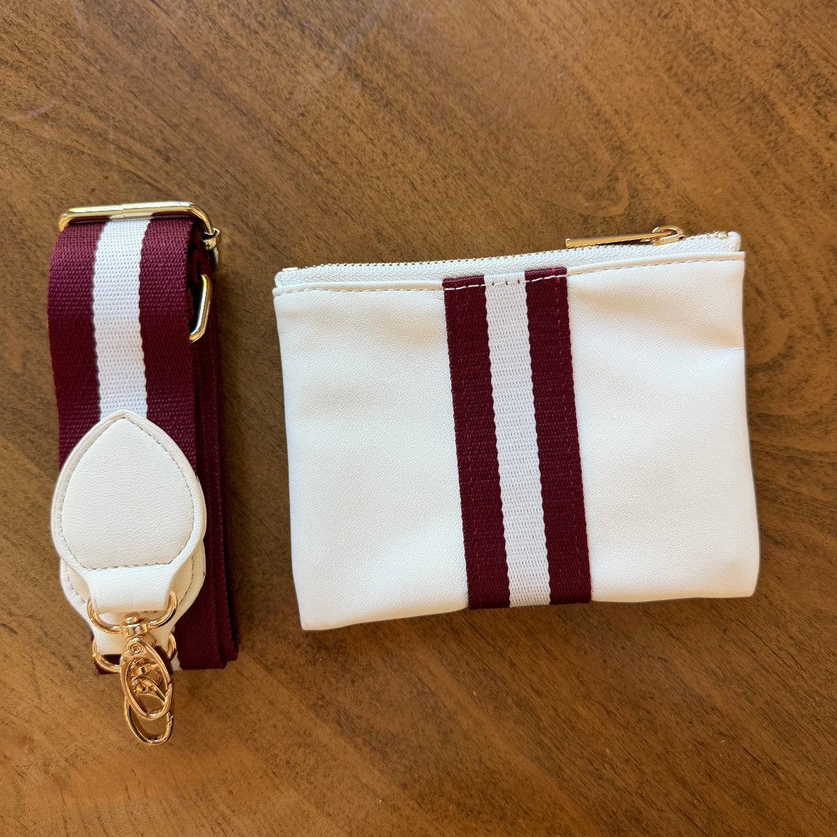 A white zippered accessory pouch with two vertical maroon stripes and a matching adjustable strap with gold-tone hardware.