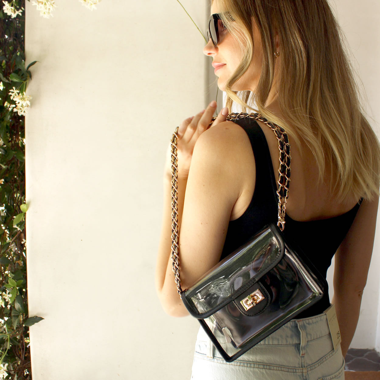 Woman casually holding a black stadium-approved purse over her shoulder by the black and gold chain