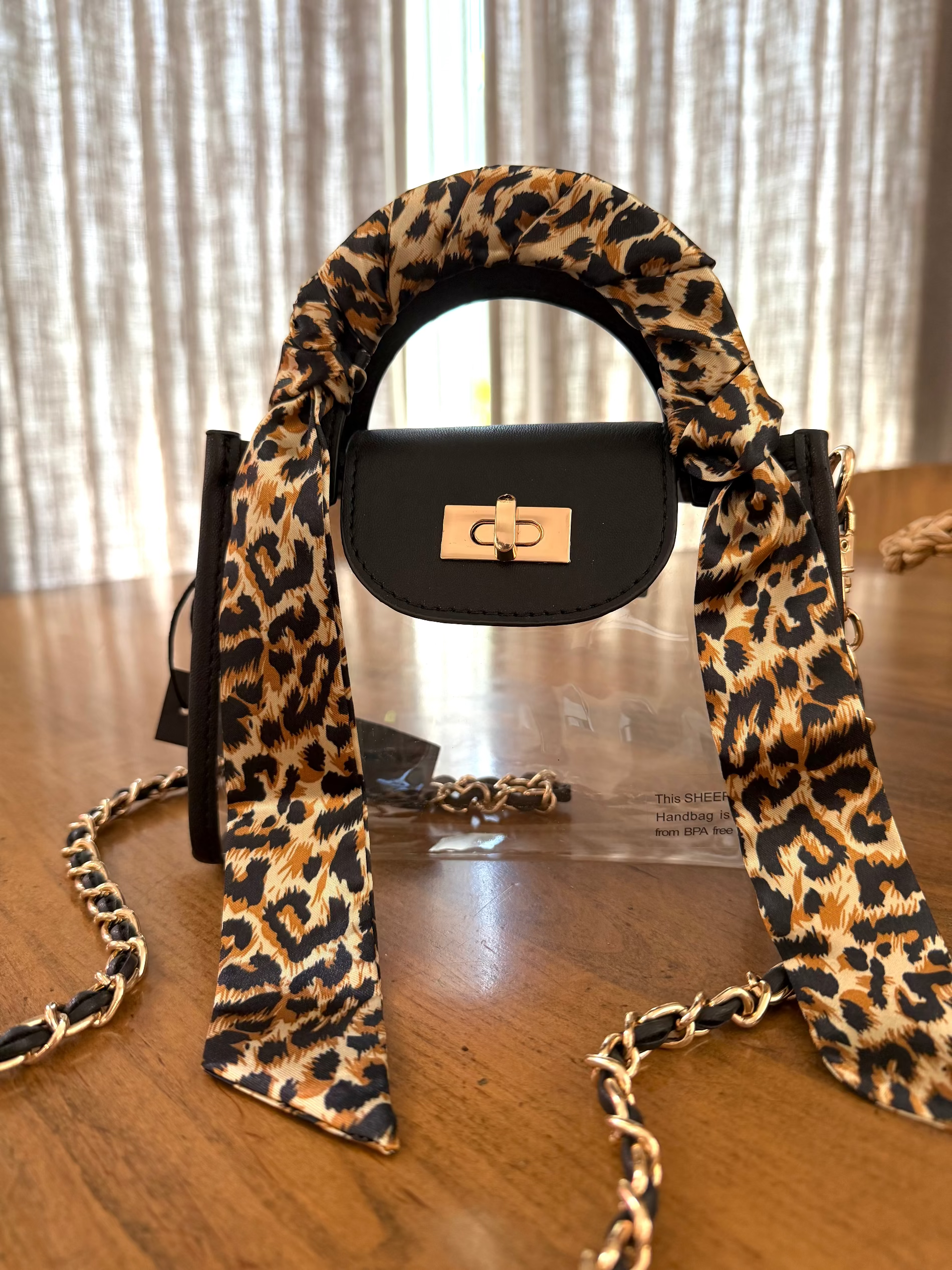 A stadium compliant black handbag with a gathered animal-print bag scarf , a gold-tone turn-lock clasp, and a black-and-gold chain strap. 