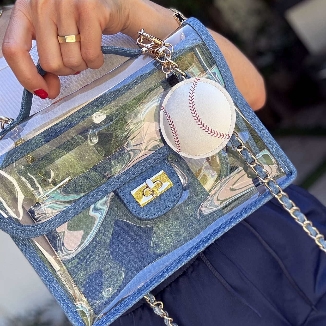 Large baseball handbag charm made of faux leather attached to a blue denim, stadium approved purse.