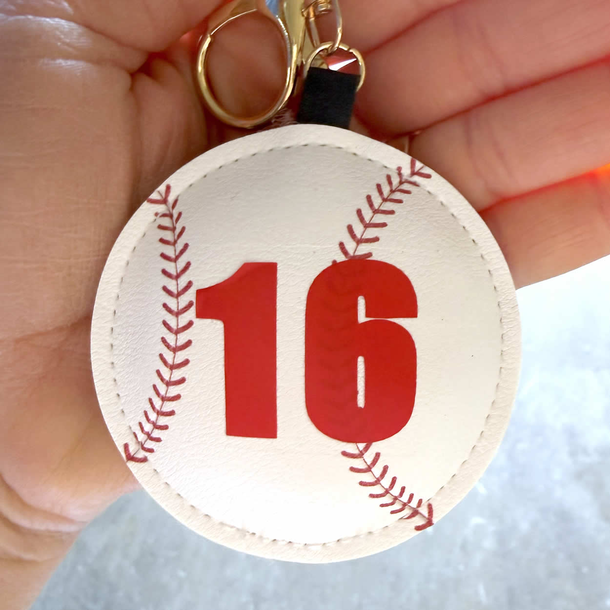 Baseball keychain with personalized number held by a hand to show size and scale.