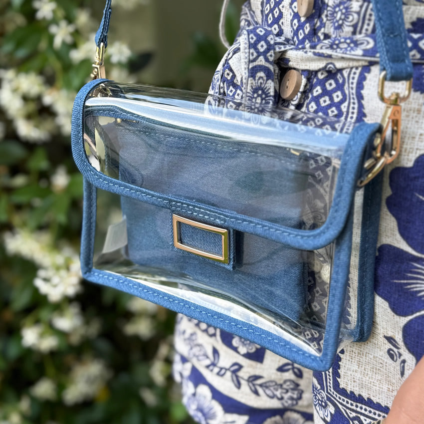 Woman in a blue and white linen outfit holding a denim-trim purse with a gold buckle.