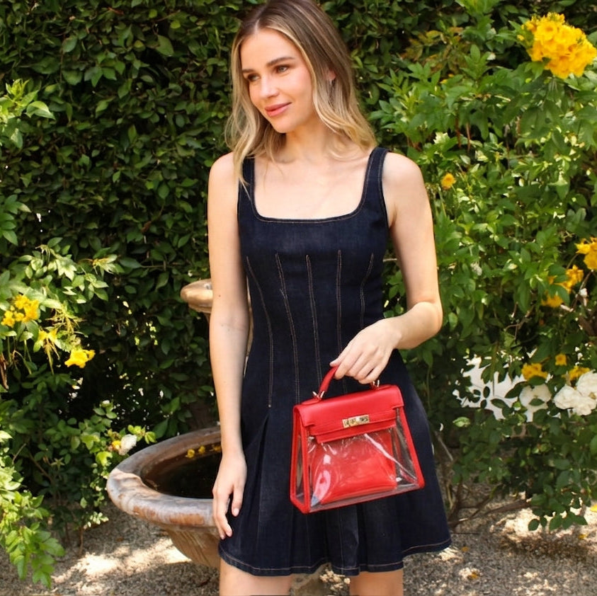 A red stadium compliant fashion purse held by a young woman in a denim dress.