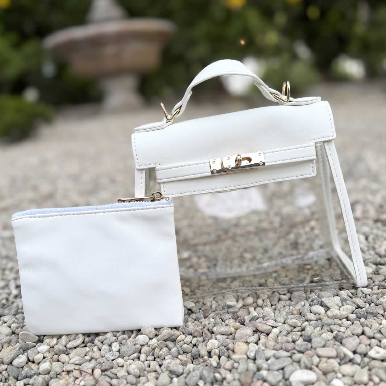 Elegant, white stadium-approved purse with gold lock , top handle, and clear sides.