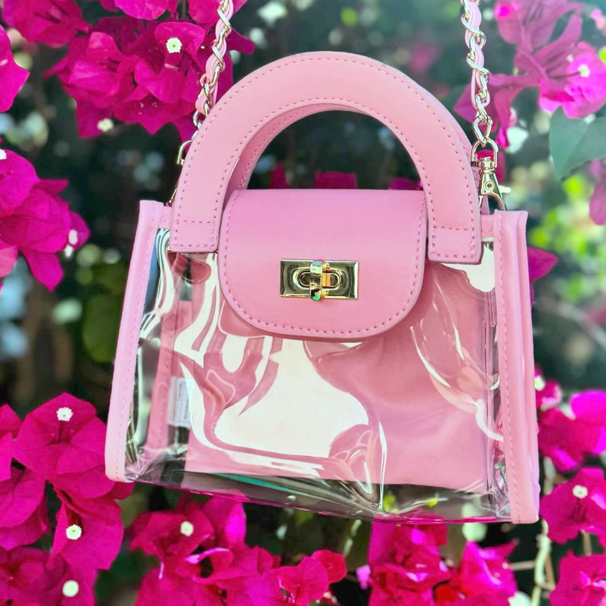 clear, stadium-approved fashion purse with pink faux-leather trim handing in a blooming pink bougainvillea bush