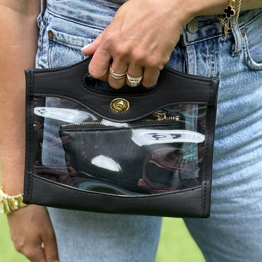 Person holding a black transparent purse with gold accents.