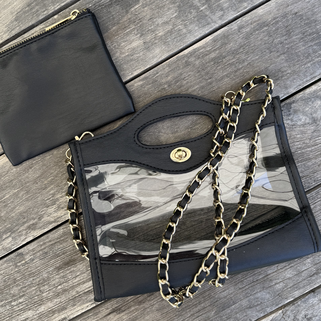 Stadium approved purse with black trim and handle laying flat with a gold chain wrapped ontop.
