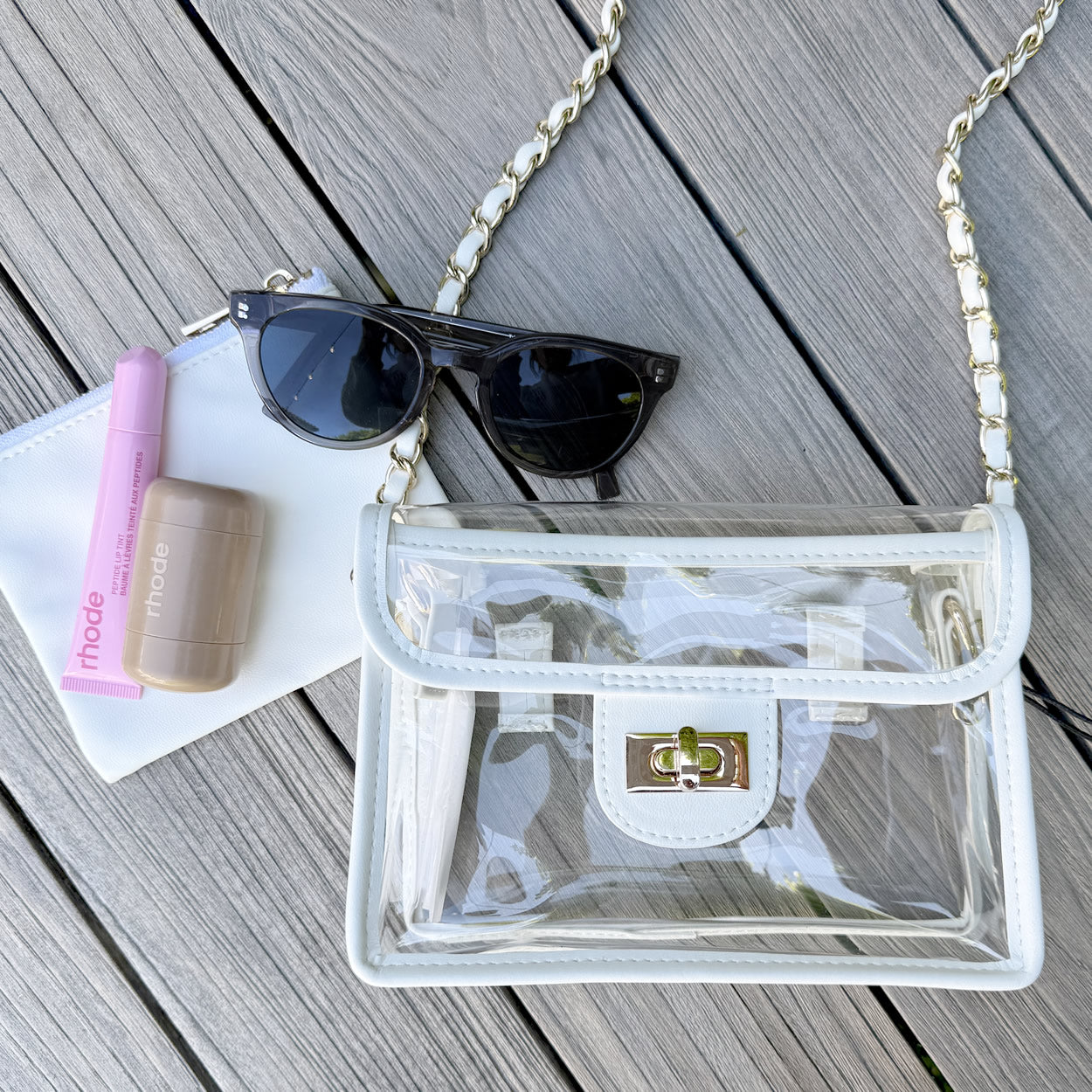 Clear, stadium approved handbag with gold chain containing sunglasses and other items.